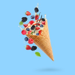 Image of Yummy ice cream ball in wafer cone and berries in air on light blue background