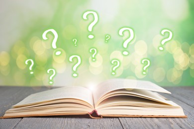 Image of Question marks and magic lights flying out of open book on table against blurred background