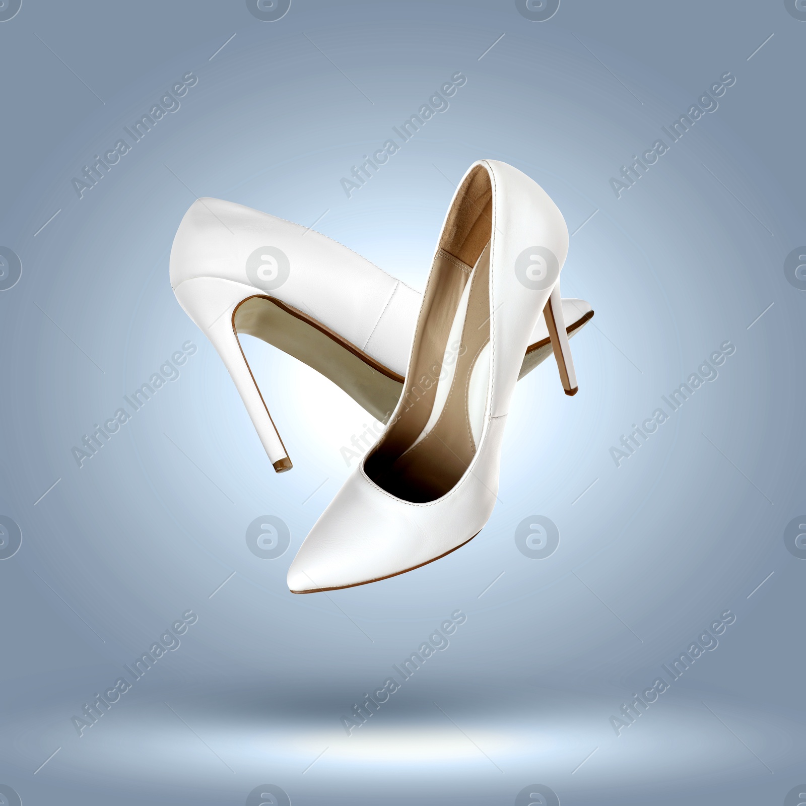 Image of Fashionable white high heel shoes in air on blue grey gradient background