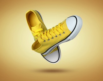 Image of Stylish yellow sneakers in air on golden gradient background