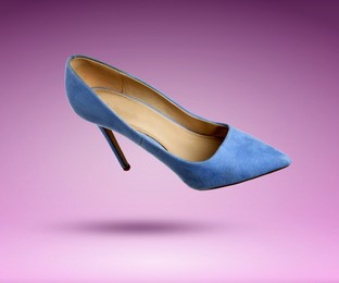 Image of Stylish blue high heeled shoe in air on purple gradient background