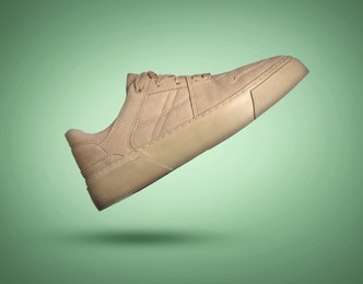 Image of Fashionable beige sneaker in air on green gradient background
