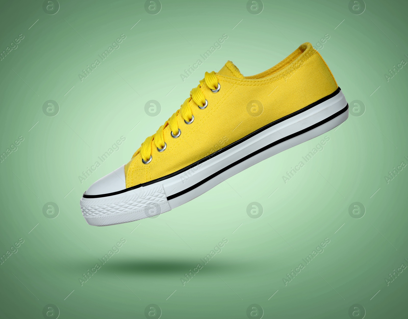 Image of Fashionable yellow sneaker in air on green gradient background