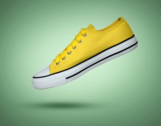 Image of Fashionable yellow sneaker in air on green gradient background