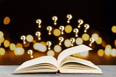Image of Question marks above open book on table against black background with blurred lights