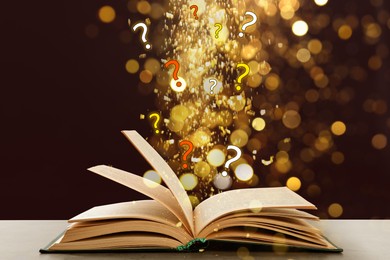 Image of Question marks and magic lights flying out of open book on table against dark background