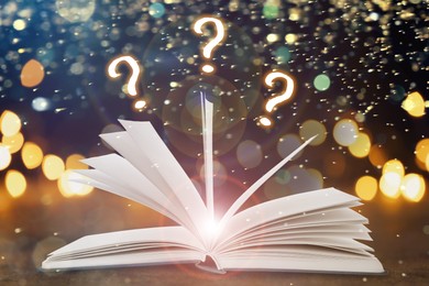 Image of Question marks above open book on table against black background with blurred lights