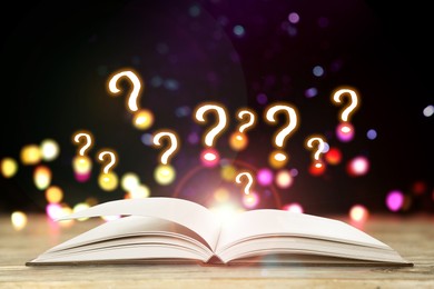 Image of Question marks above open book on table against black background with blurred lights