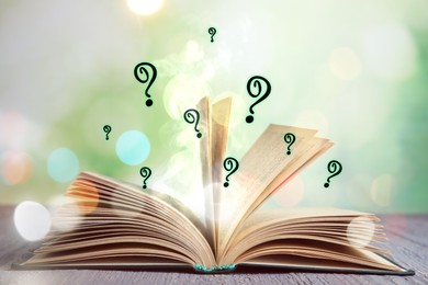 Image of Question marks and magic lights flying out of open book on table against blurred background