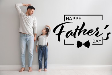 Image of Happy Father's Day. Little girl and daddy measuring their height near light grey wall indoors