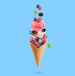 Image of Yummy ice cream balls in wafer cone and berries in air on light blue background