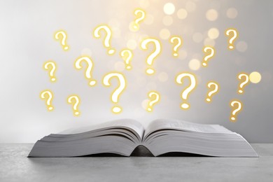 Image of Question marks above open book on table against grey background with blurred lights