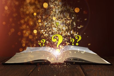 Image of Question marks and magic lights flying out of open book on table against dark background