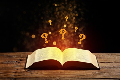 Image of Question marks and magic lights flying out of open book on table against black background