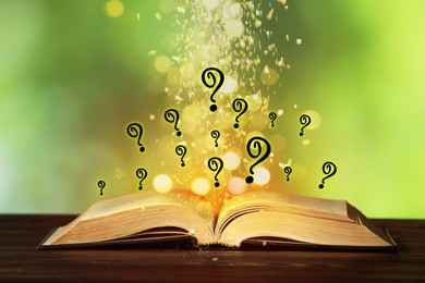Image of Question marks and magic lights flying out of open book on table against blurred green background