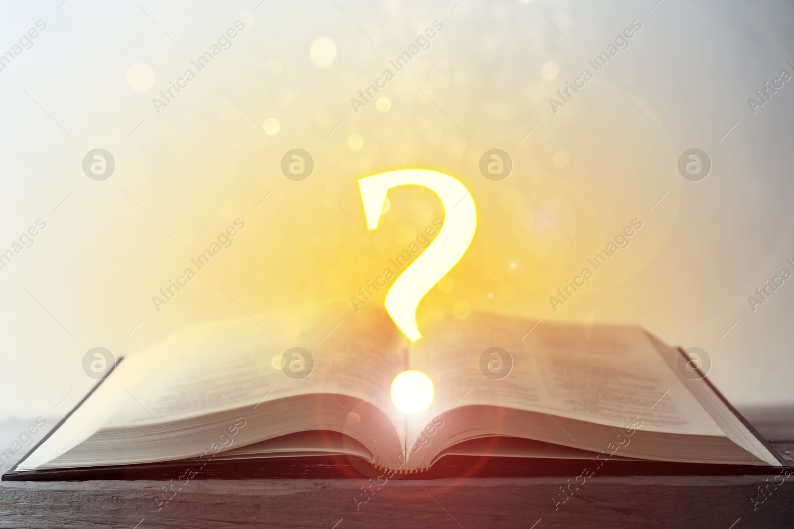 Question mark and magic lights above open book on table against light background Image of Question mark and magic lights above open book on table against light background