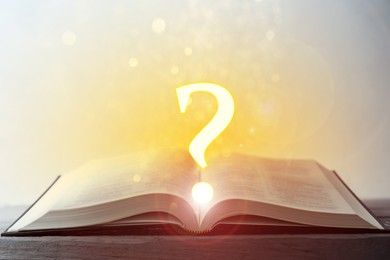 Image of Question mark and magic lights above open book on table against light background