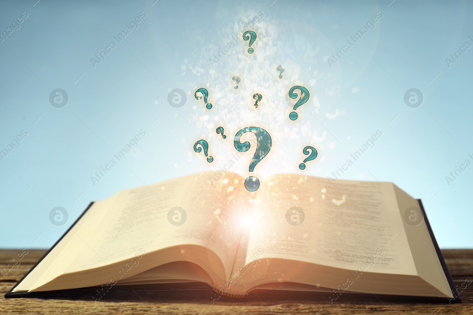Question marks and lights flying out of open book on table against light blue background Image of Question marks and lights flying out of open book on table against light blue background