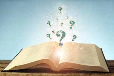 Image of Question marks and lights flying out of open book on table against light blue background