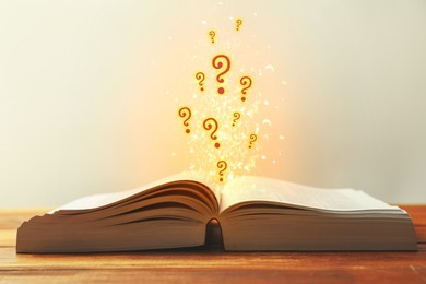 Image of Question marks and lights flying out of open book on table against light background