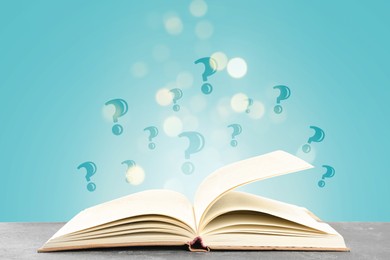 Image of Question marks above open book on table against light blue background with blurred lights