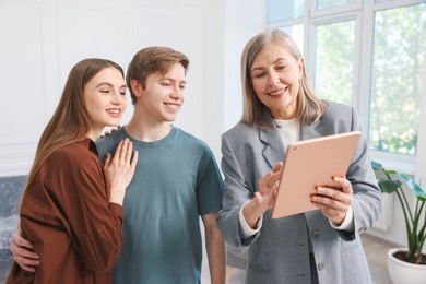 Photo of Smiling real estate agent with tablet working with couple at home