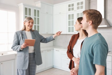Photo of Smiling real estate agent with tablet working with couple in kitchen
