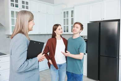 Photo of Real estate agent with clipboard working with couple in kitchen