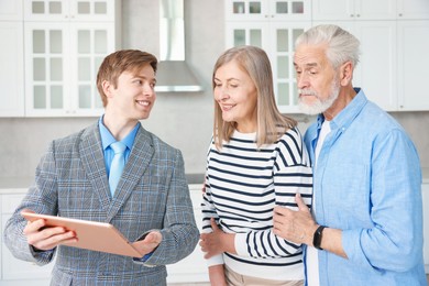 Photo of Smiling real estate agent with tablet working with couple in kitchen