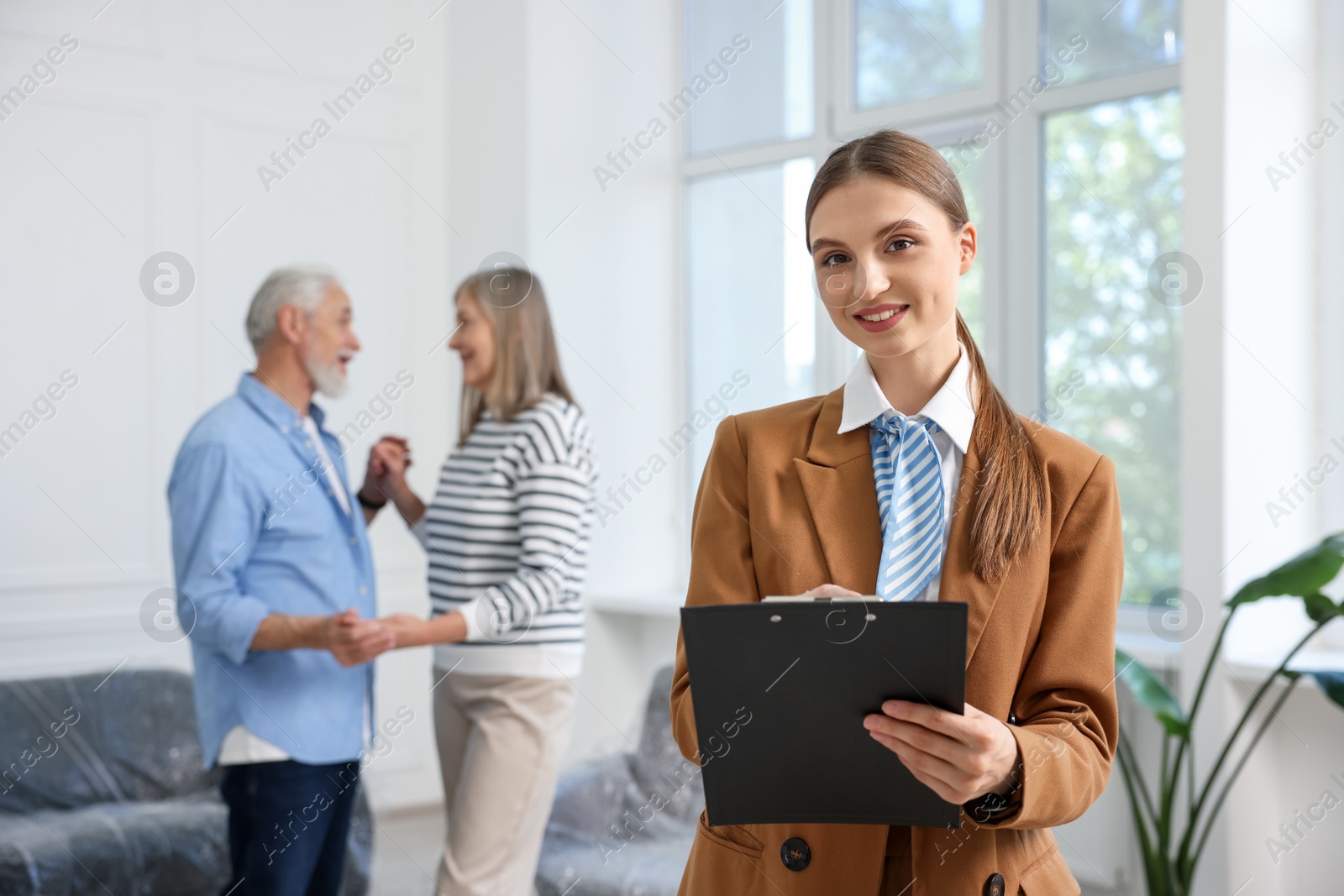 Smiling real estate agent with clipboard and couple at home, selective focus Photo of Smiling real estate agent with clipboard and couple at home, selective focus