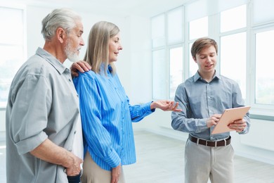 Photo of Smiling real estate agent with tablet working with couple at home
