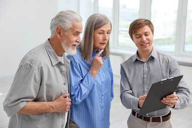 Photo of Smiling real estate agent with clipboard working with couple at home
