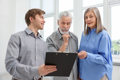 Photo of Smiling real estate agent with clipboard working with couple at home