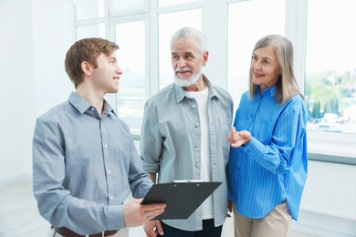 Photo of Smiling real estate agent with clipboard working with couple at home