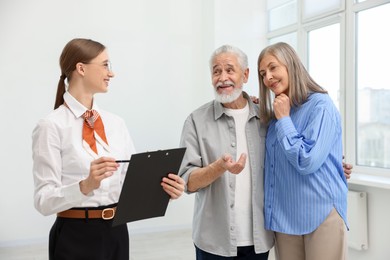 Photo of Smiling real estate agent with clipboard working with couple at home