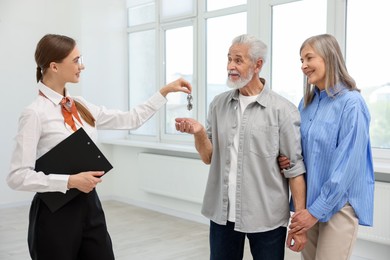 Photo of Smiling real estate agent with clipboard giving house key to new owner at home