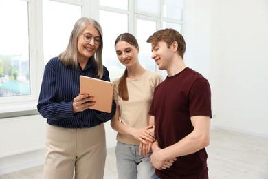 Photo of Smiling real estate agent with tablet working with couple at home