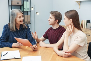 Photo of Real estate agent with tablet working with couple at table in office