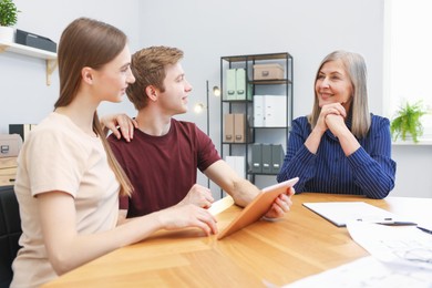 Photo of Smiling real estate agent and couple with tablet at table in office
