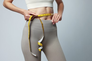 Photo of Woman measuring her belly with tape on gray background, closeup