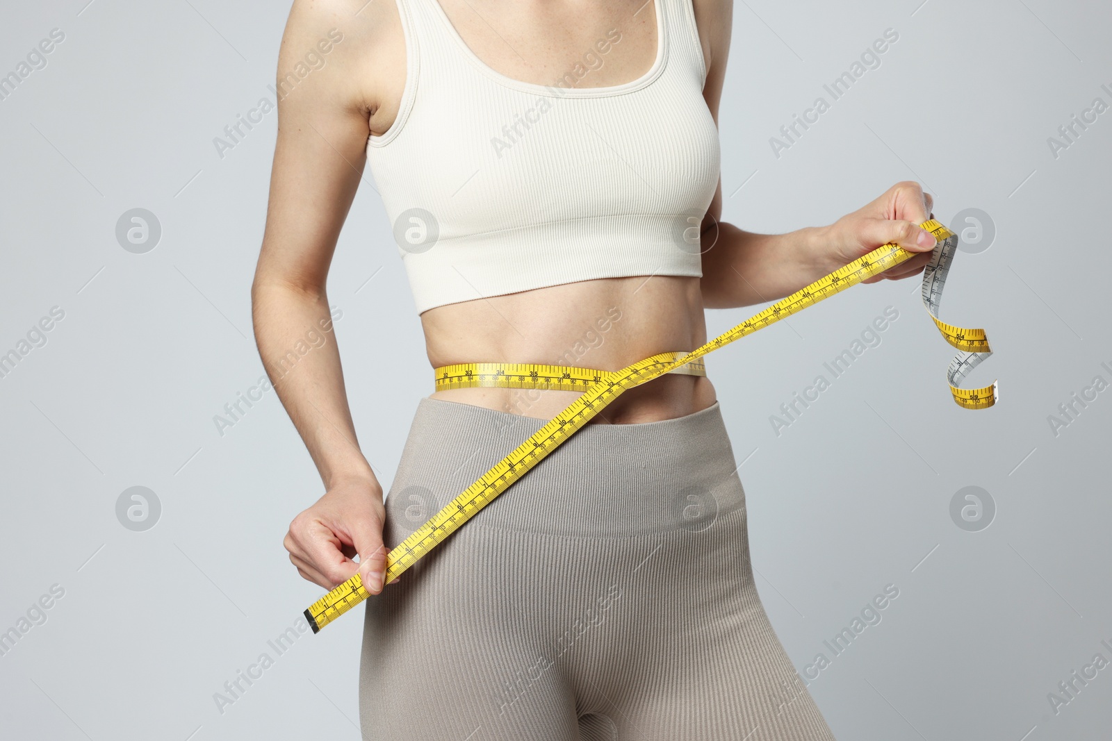 Woman measuring her belly with tape on gray background, closeup Photo of Woman measuring her belly with tape on gray background, closeup