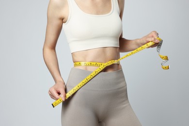 Photo of Woman measuring her belly with tape on gray background, closeup