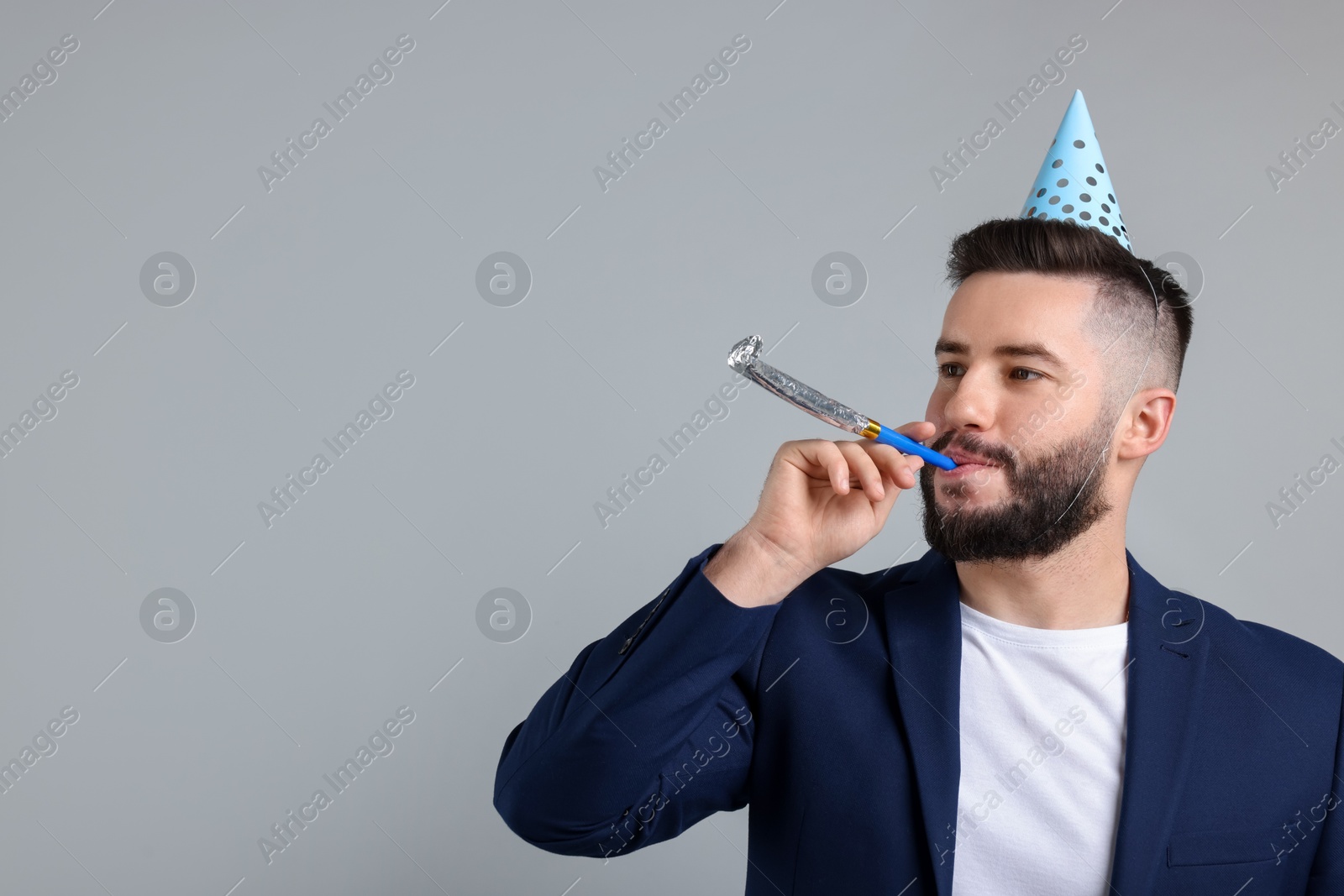 Happy Birthday. Handsome man with party hat and blower on grey background, space for text Photo of Happy Birthday. Handsome man with party hat and blower on grey background, space for text
