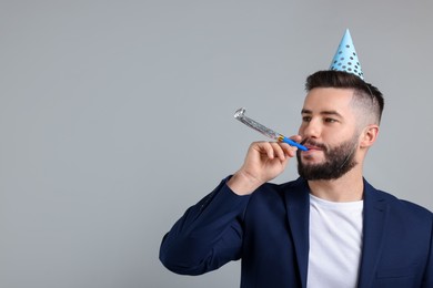 Photo of Happy Birthday. Handsome man with party hat and blower on grey background, space for text
