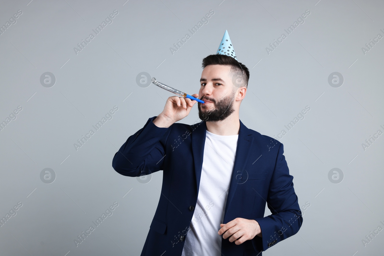 Happy Birthday. Handsome man with party hat and blower on grey background Photo of Happy Birthday. Handsome man with party hat and blower on grey background