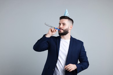 Photo of Happy Birthday. Handsome man with party hat and blower on grey background