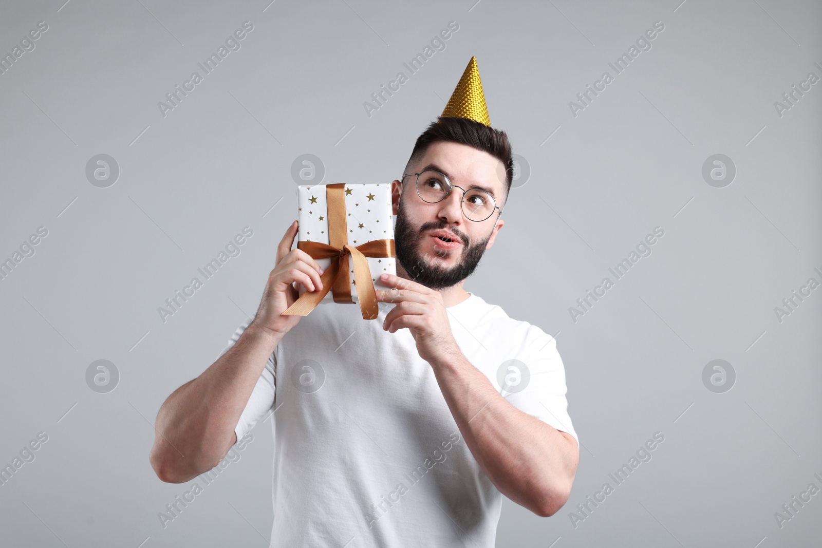 Happy Birthday. Handsome man with party hat and gift box on grey background Photo of Happy Birthday. Handsome man with party hat and gift box on grey background