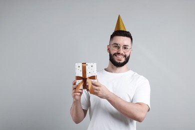 Photo of Happy Birthday. Handsome man with party hat and gift box on grey background, space for text