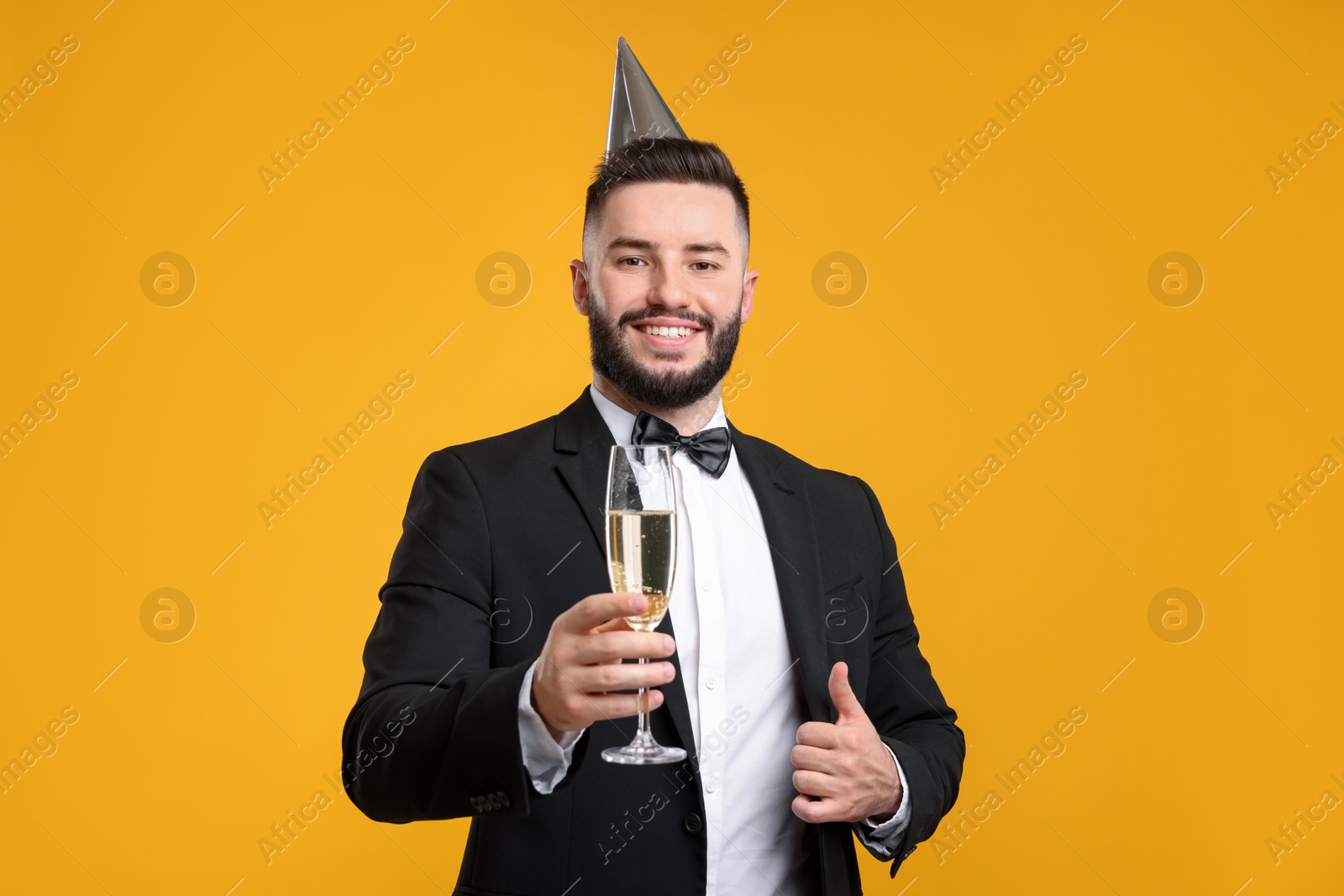 Happy Birthday. Handsome man with party hat and champagne showing thumbs up on orange background Photo of Happy Birthday. Handsome man with party hat and champagne showing thumbs up on orange background