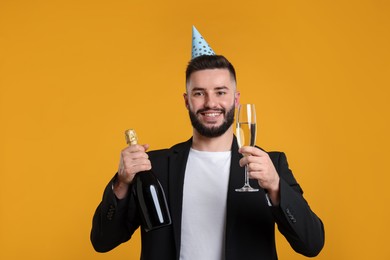 Photo of Happy Birthday. Handsome man with party hat and champagne on orange background